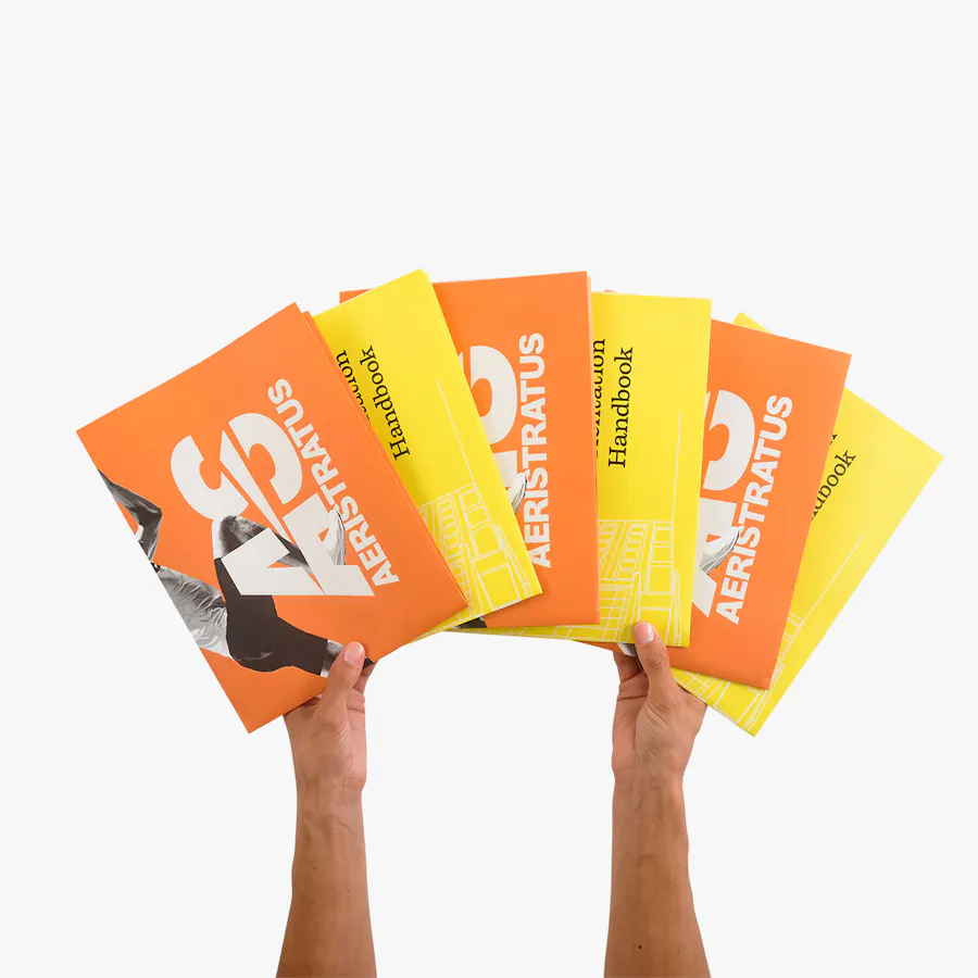 Two hands holding six folded posters in yellow and orange fanned out.